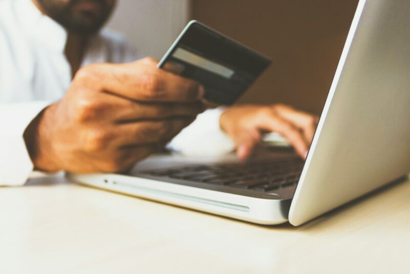 A person holding a bank card in front of a laptop