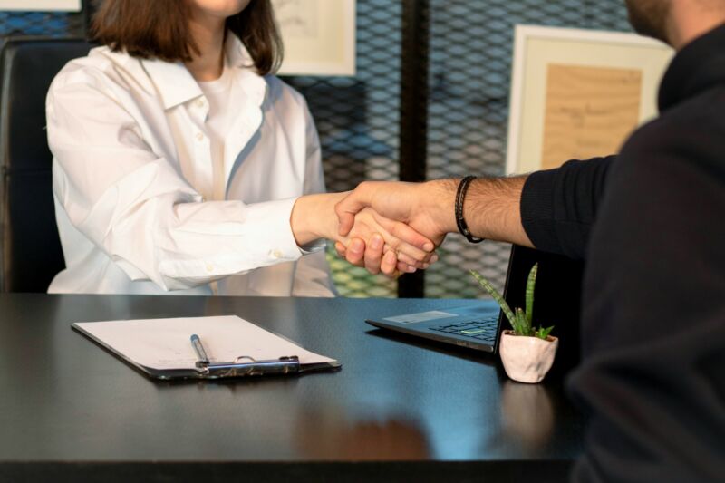 A man and woman shaking hands across a desk