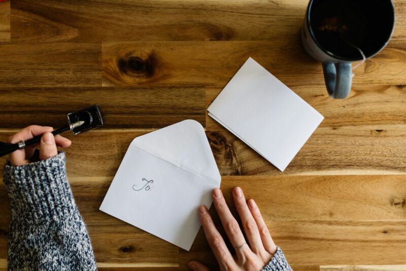 A person writing a letter beside a cup of coffee