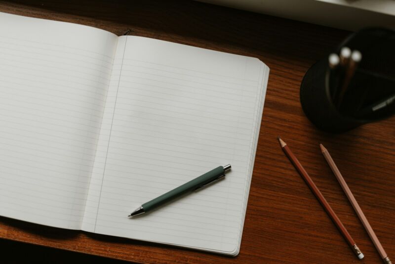 An open notebook with pens on a wooden desk