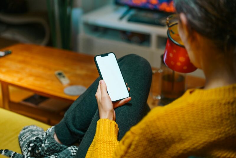 A woman on a cozy sofa using her phone with a warm drink