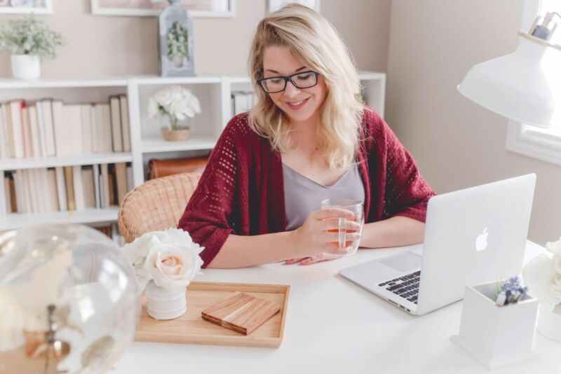 A smiling woman with a mug beside her laptop at home