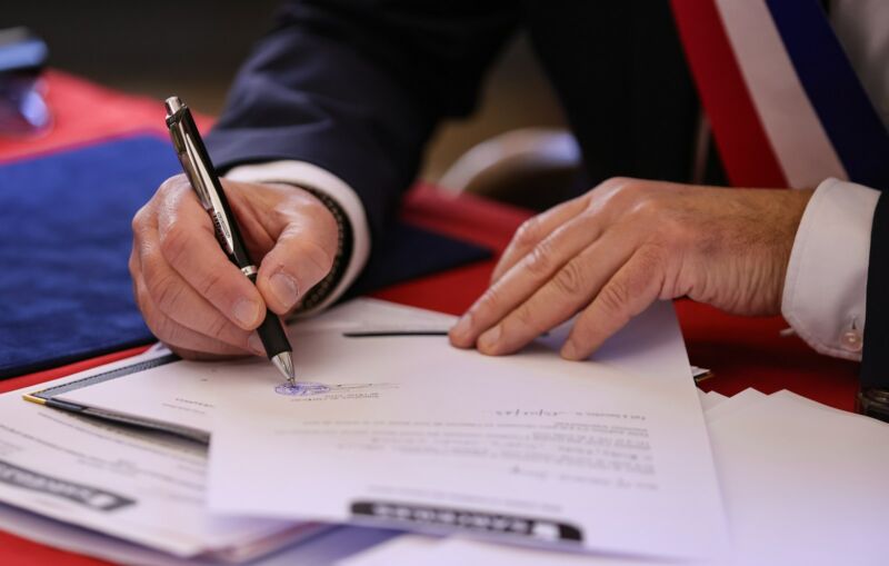 A hand signing a document with a pen