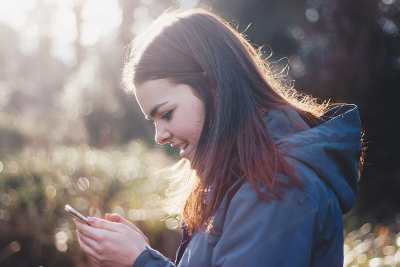 A woman smiling at her phone outdoors